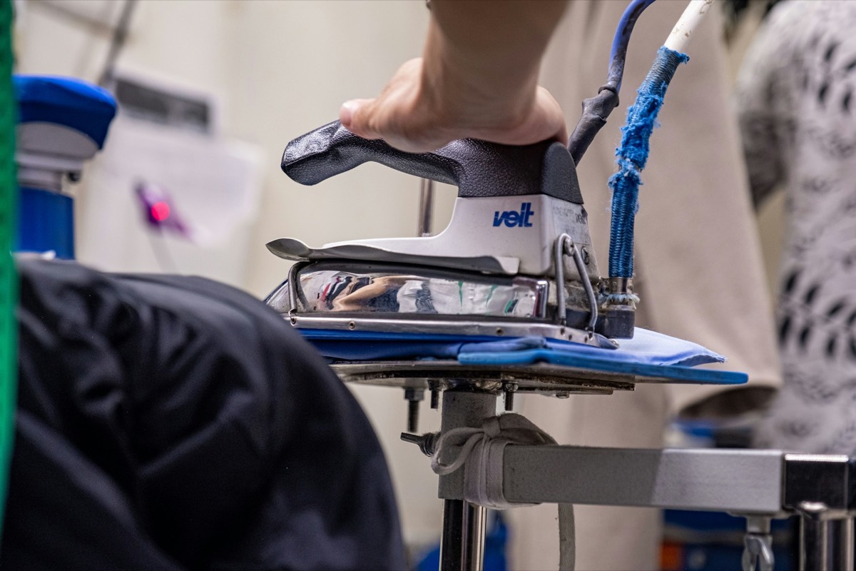A hand guiding a professional steam iron over a garment on a pressing table