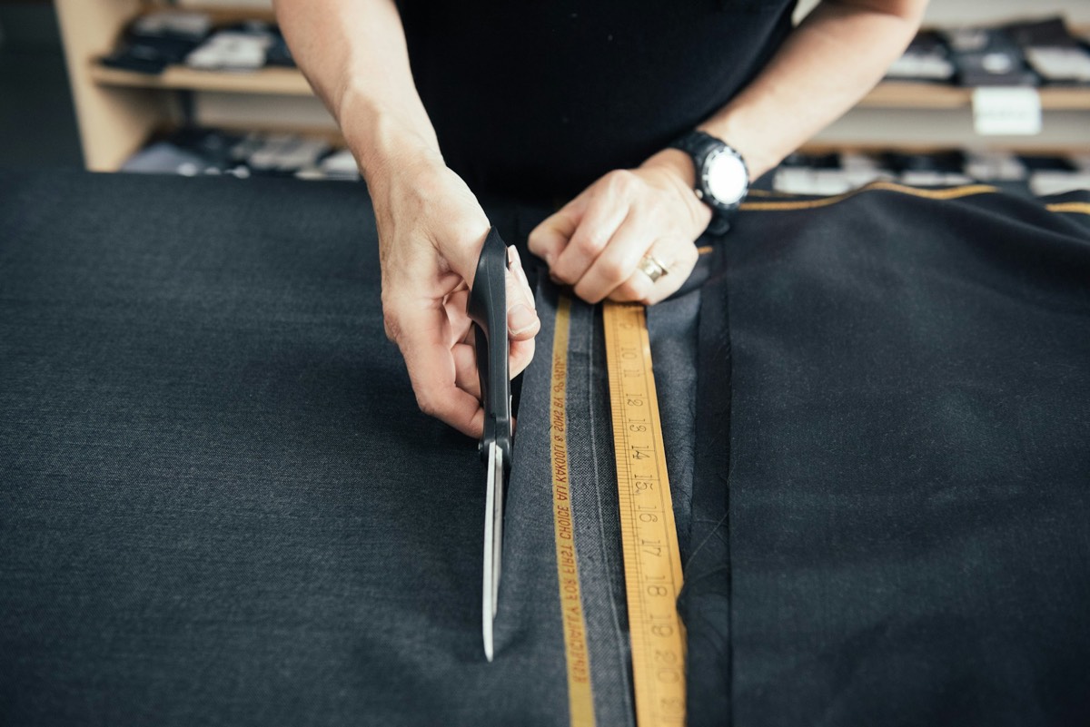 A tailor cutting charcoal suit cloth along a measuring tape