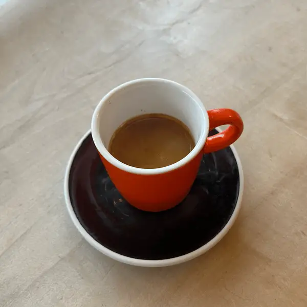 A double espresso in an orange cup on a dark saucer