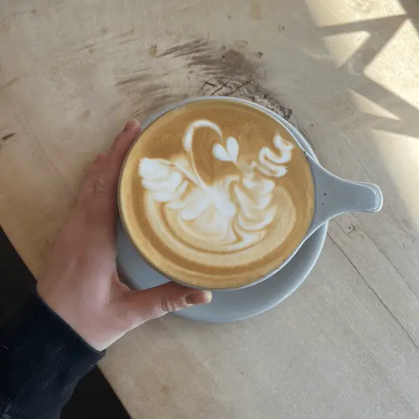 A latte with swan latte art, held over the wooden counter
