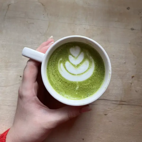 A green matcha latte with a rosetta, held in both hands