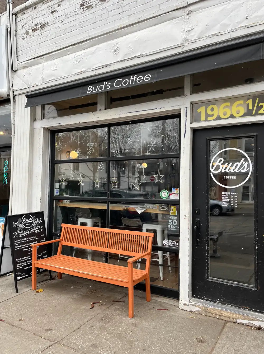 The front of Bud's Coffee: a black awning, the number 1966½ in gold over the door, and an orange bench under the window