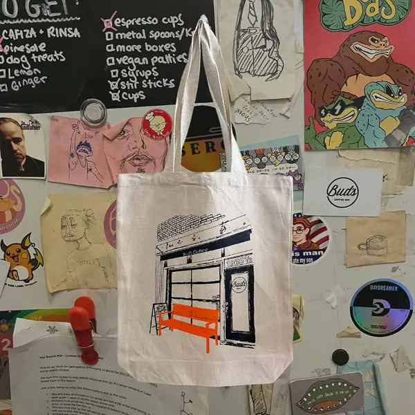 A canvas tote printed with a drawing of the Bud's shopfront and its orange bench