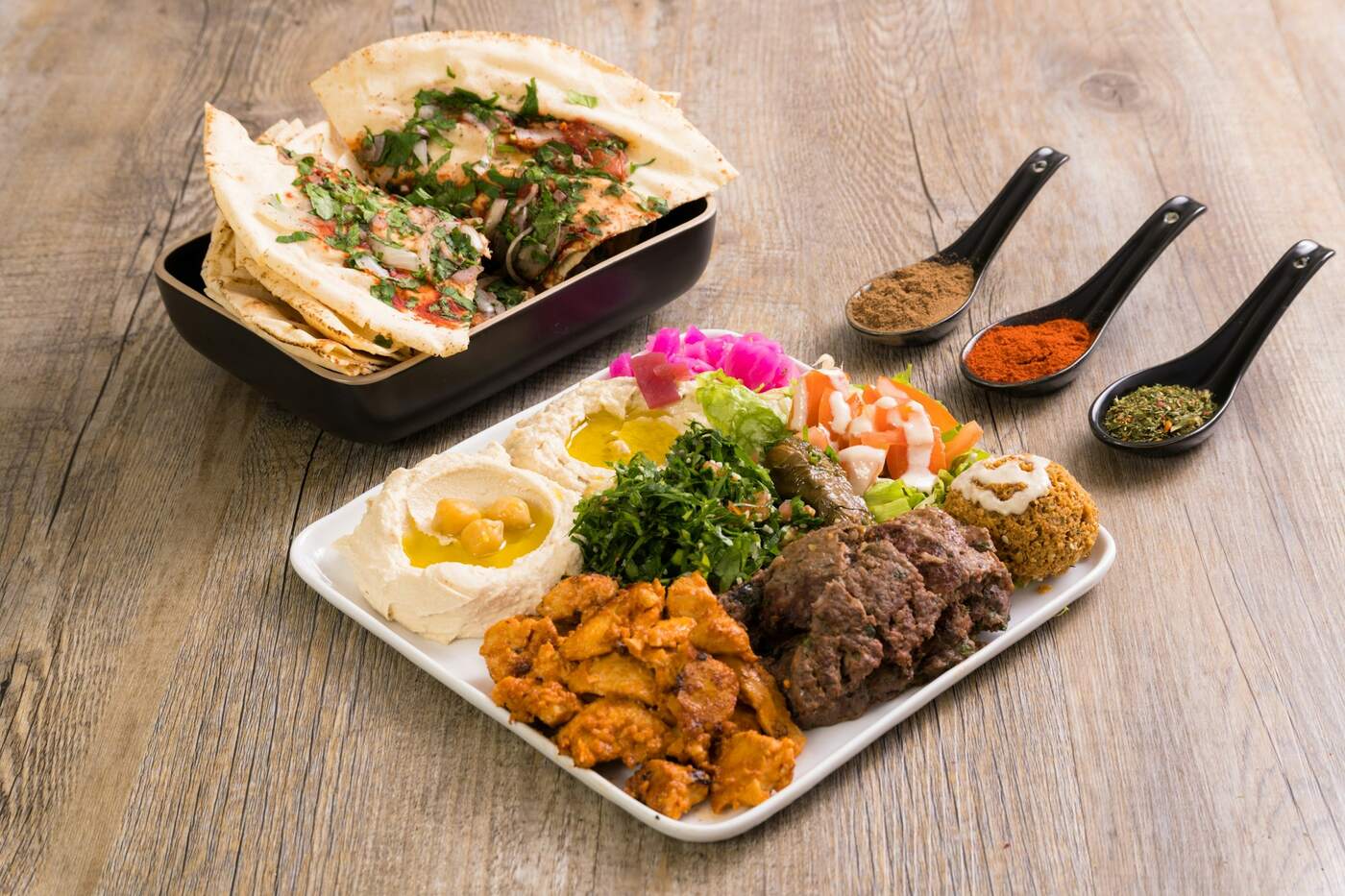 A plate of chicken and beef shawarma with hummus, tabbouleh, falafel and pita