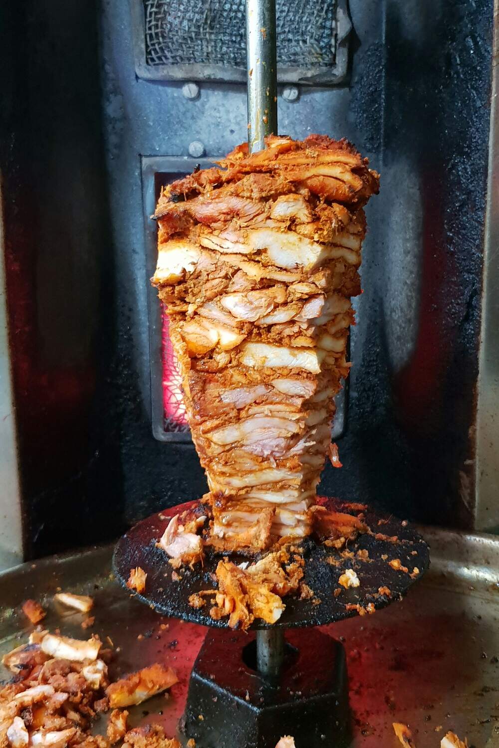 A cone of chicken shawarma turning in front of a glowing grill
