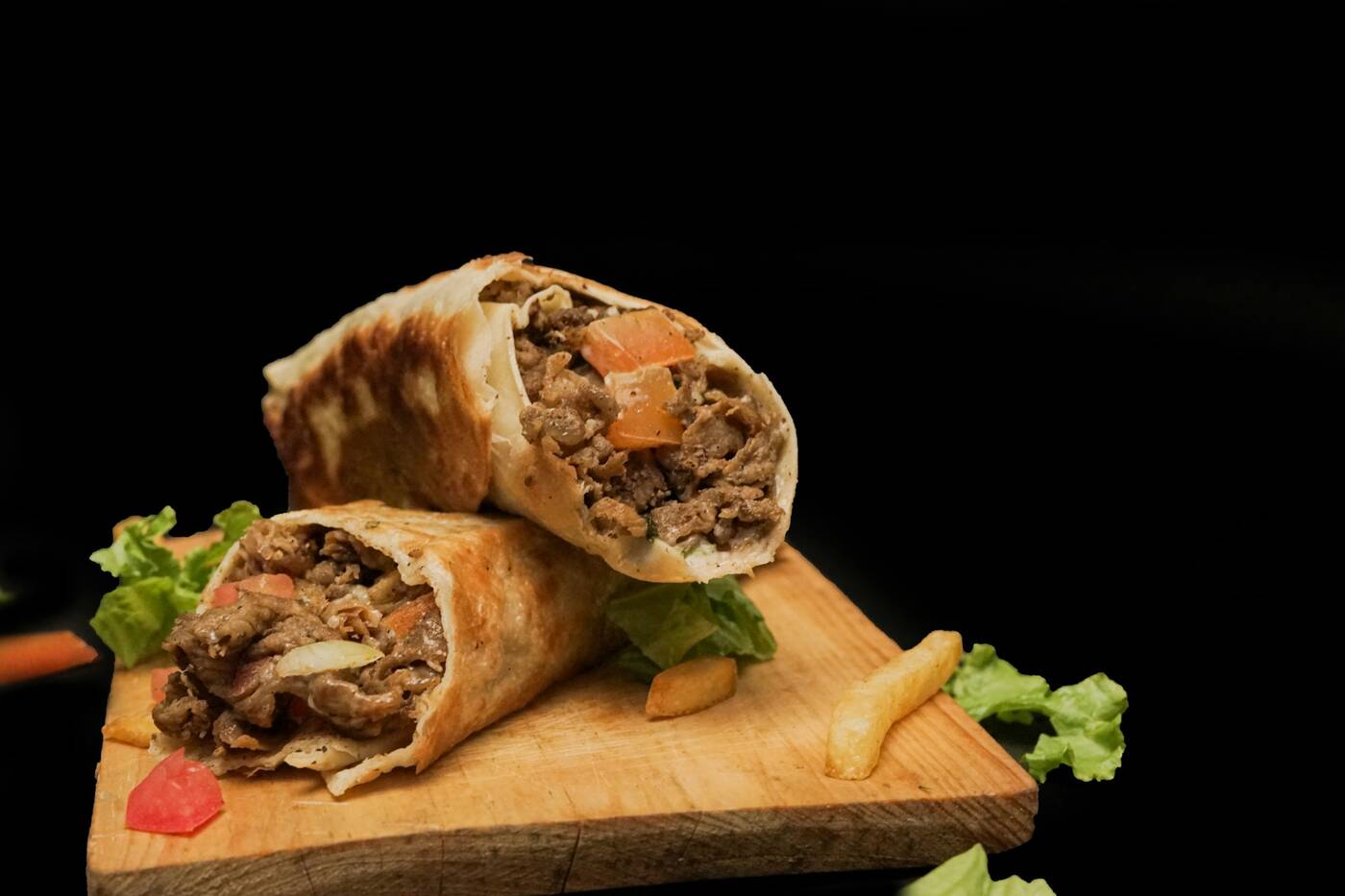 Two halves of a beef shawarma wrap with tomato and lettuce on a wooden board
