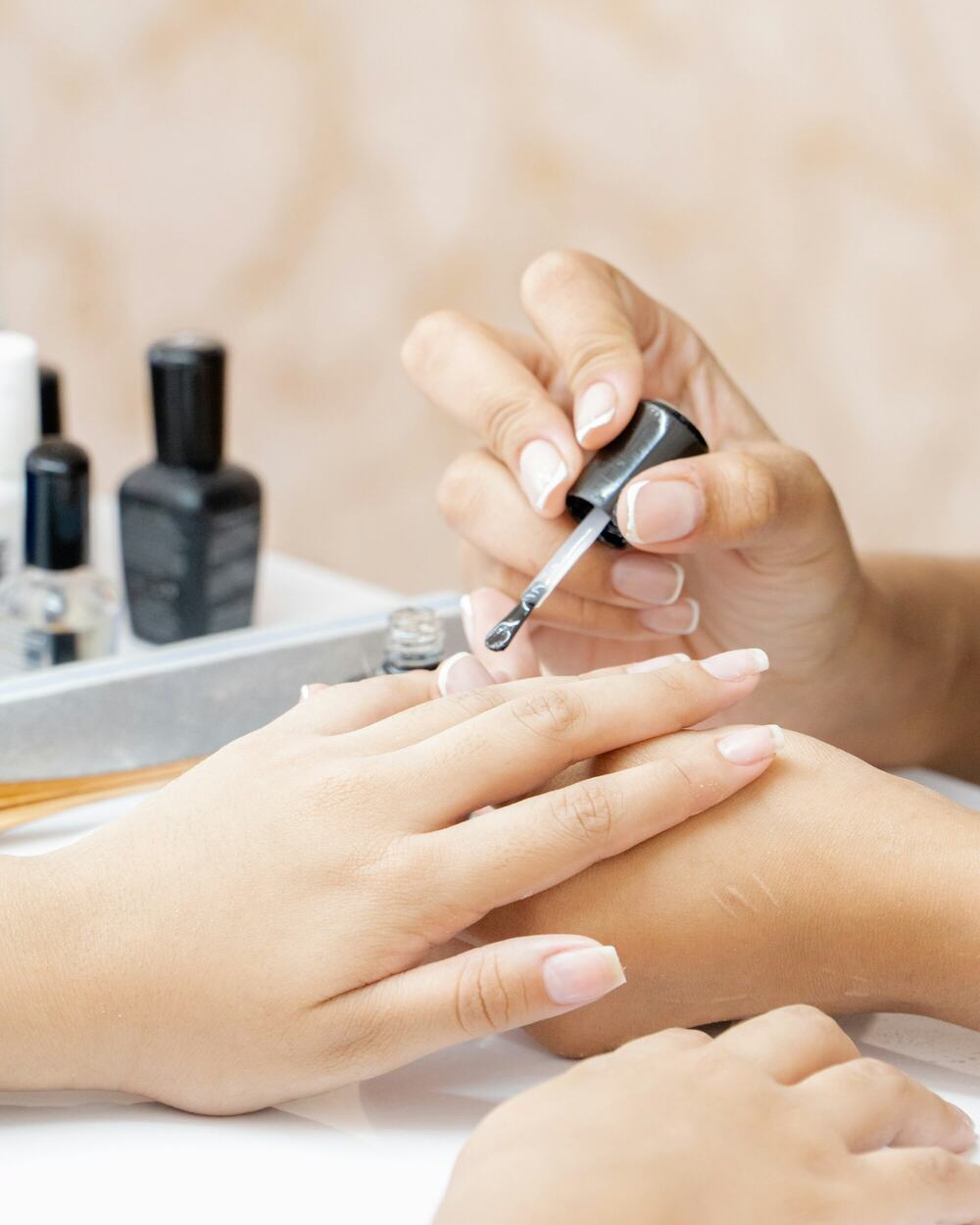 A manicurist brushing pale polish onto a client's nails