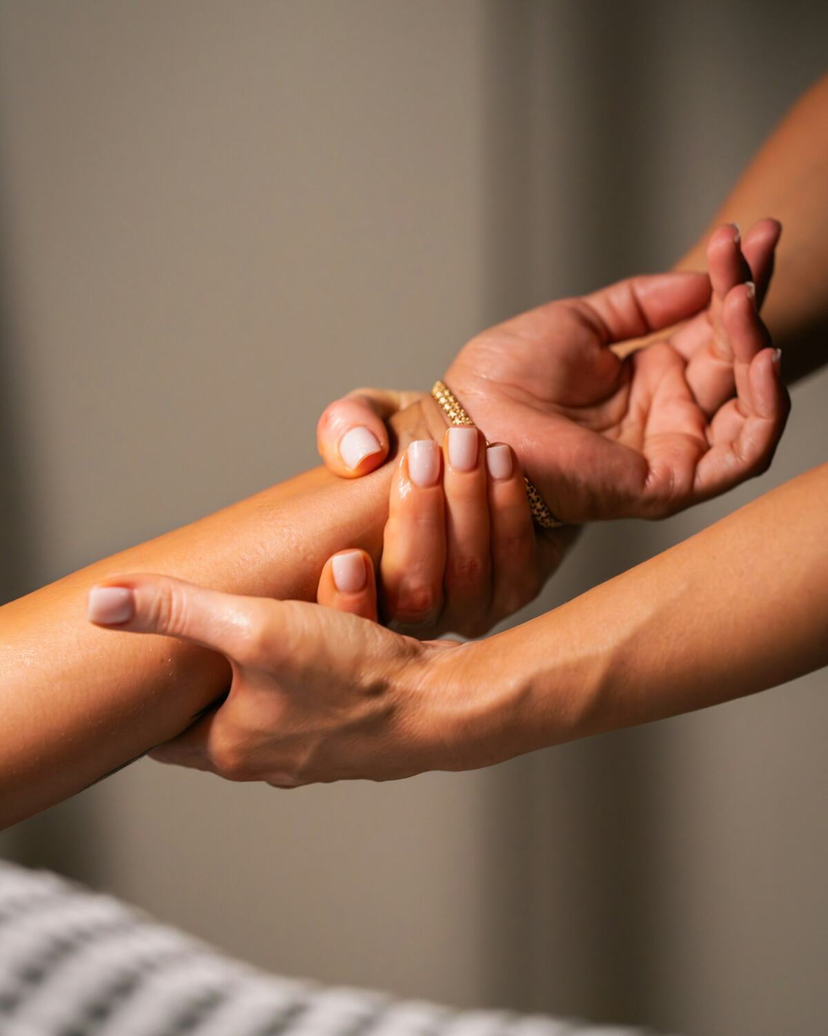 An esthetician's hands massaging a client's forearm and hand on a treatment bed