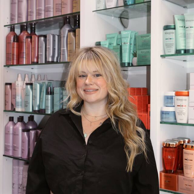 Carissa, Stylist, in front of the salon’s product wall