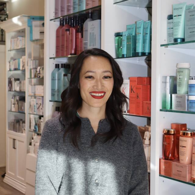 Hanh, Sr. Colourist, in front of the salon’s product wall