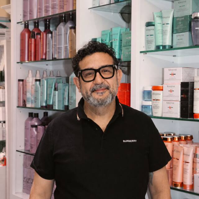 Joe, Co-owner · Sr. Stylist, in front of the salon’s product wall