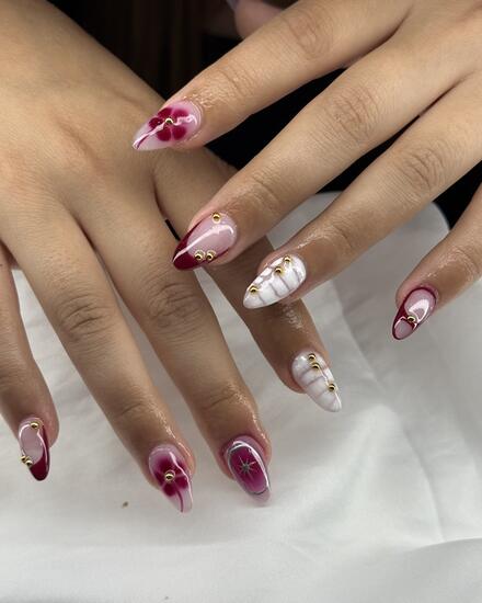 Almond nails with burgundy watercolour blooms, gold studs and a white ribbed accent