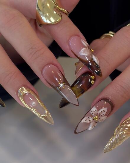 Stiletto nails mixing gold chrome, tortoiseshell, pearls and a painted white flower