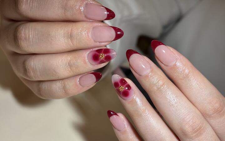 Sheer pink almond nails with deep red French tips and red aura blooms