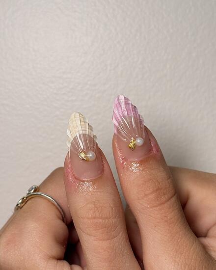 Two almond nails sculpted as seashells, one white and one pink, each set with a pearl