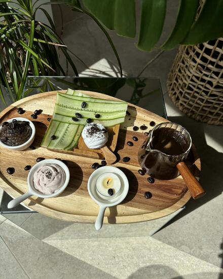 A spa treatment tray with cucumber slices, coffee beans, a lit candle and small bowls