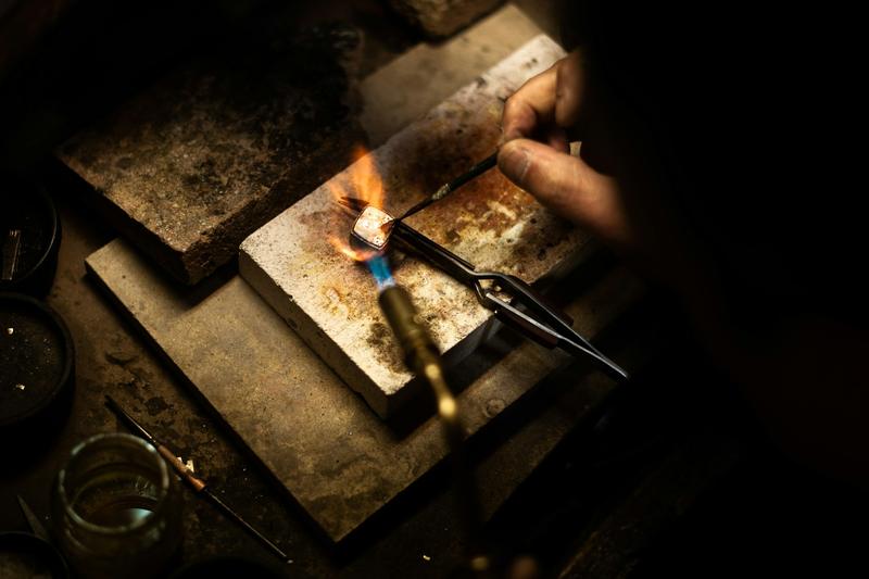A jeweller's hand holding a small piece in a torch flame at the bench