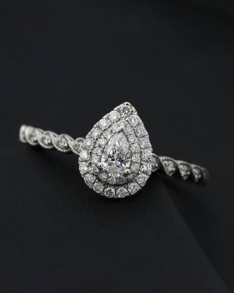 A pear-shaped diamond ring with a halo of small stones on a dark surface