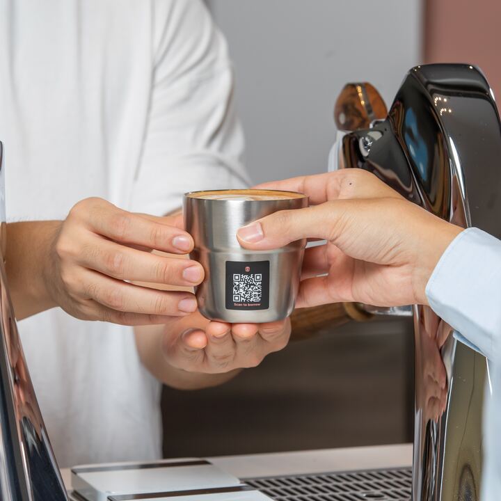 A barista hands a Muuse cup with a QR code across the counter