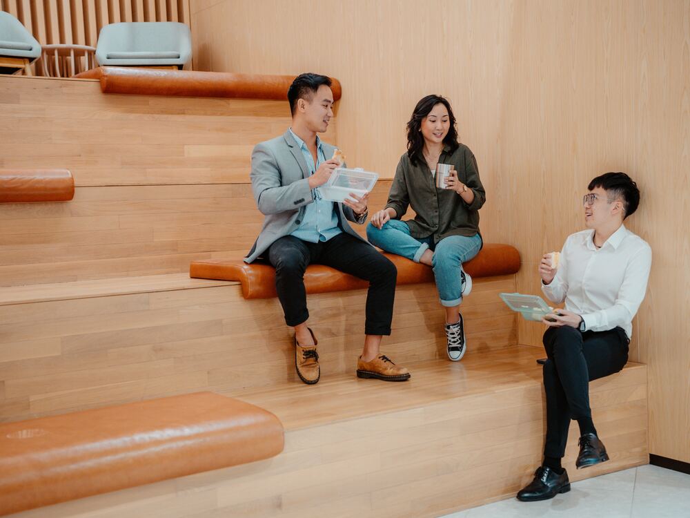 Three colleagues on wooden office steps having lunch from Muuse containers and cups