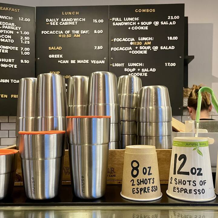 Stacks of clean Muuse cups on a café counter under the menu board