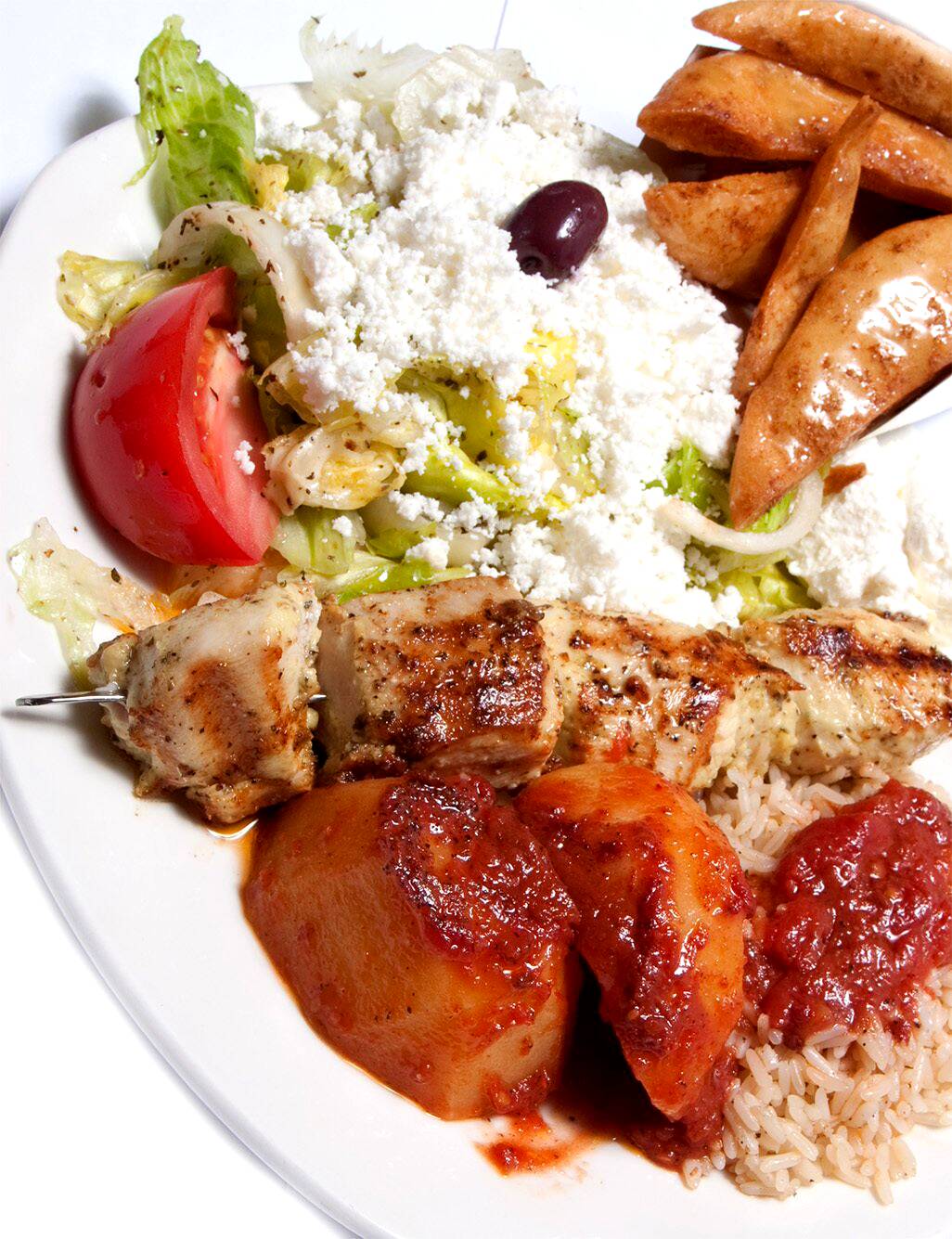 A chicken souvlaki skewer with Greek salad, potatoes, rice and pita sticks