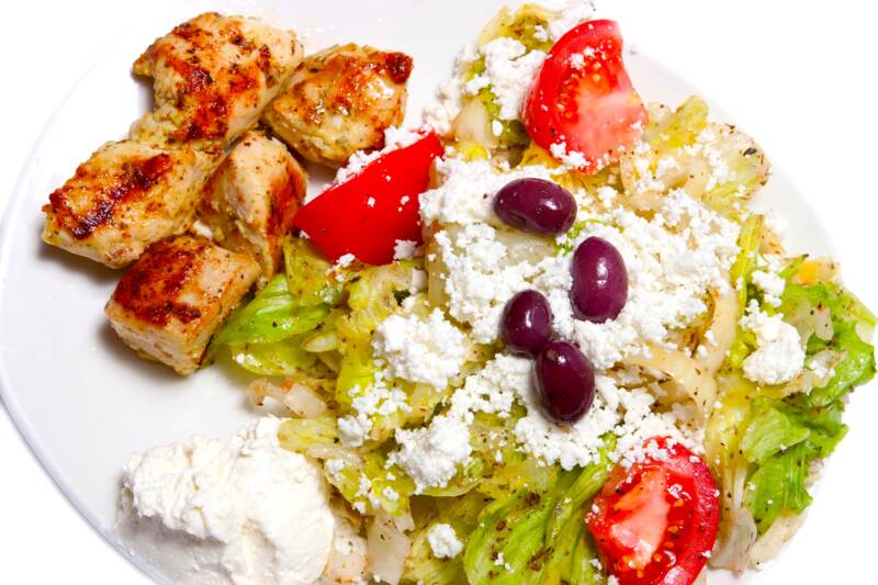 Grilled chicken souvlaki on a Greek salad with feta, kalamata olives, tomato and tzatziki