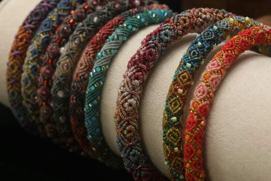 A row of knotted and beaded bangles in red, teal, purple and amber on a cream display roll