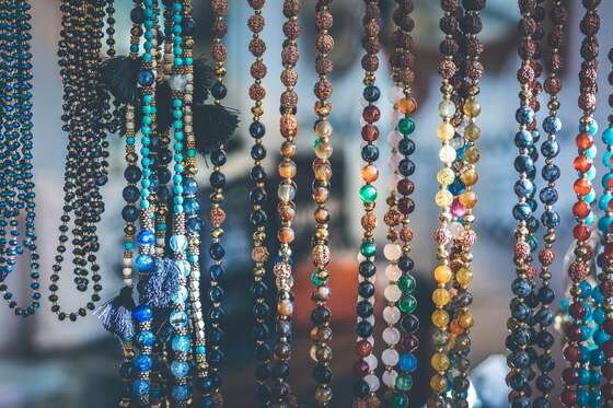Long strings of coloured stone and wooden beads hanging side by side, some with tassels