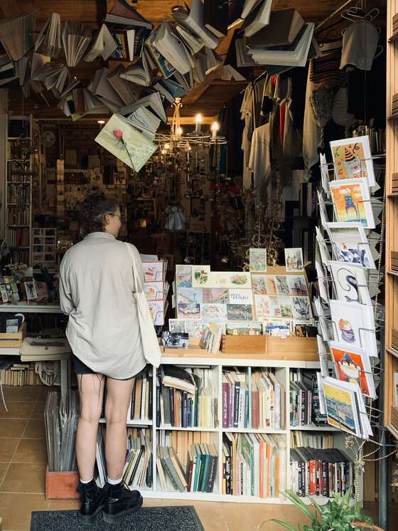 A shopper browsing a crowded little shop with cards, books and clothing, and open books hung from the ceiling