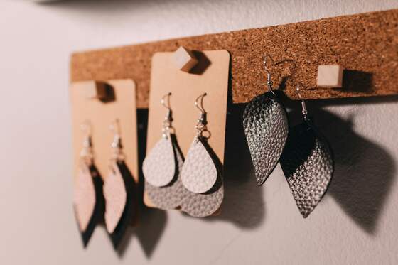 Three pairs of leaf-shaped leather earrings on kraft cards, pinned to a cork strip