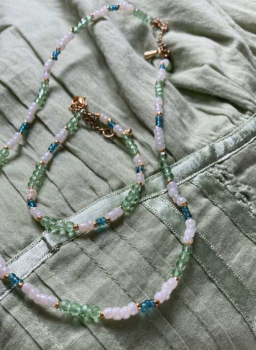 A pale pink and green glass-bead necklace and bracelet laid on a sage linen shirt