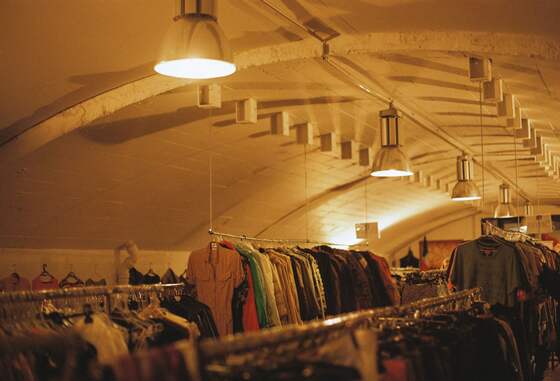 Racks of colourful shirts and jackets under warm lamps in a vaulted shop