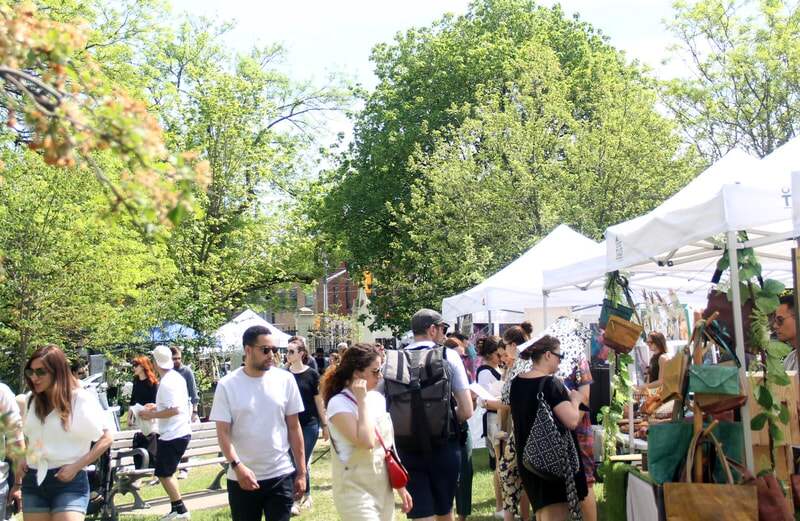 A busy path through the market, with handmade bags hanging at a white canopy booth